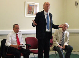 Malcolm standing to answer a question with Gordon and Mark seated on either side of him